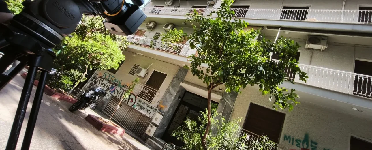 Κάμερα σε τρίποδο μπροστά σε πολυκατοικία στην Κυψέλη, με γκράφιτι…