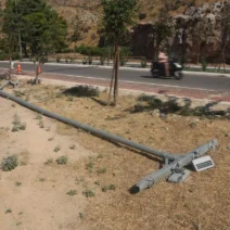 Πεσμένος στύλος φωτισμού σε ξηρό έδαφος δίπλα σε άσφαλτο, με βουνά …