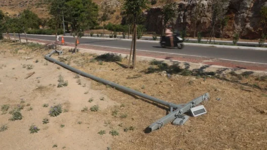Πεσμένος στύλος φωτισμού σε ξηρό έδαφος δίπλα σε άσφαλτο, με βουνά …