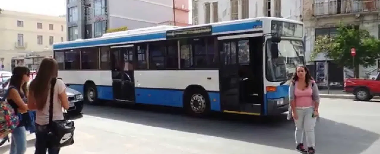 Αστικό λεωφορείο σε δρόμο της Πάτρας με πεζούς και κτίρια.