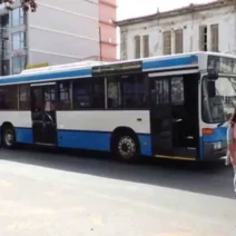 Αστικό λεωφορείο σε δρόμο της Πάτρας με πεζούς και κτίρια.