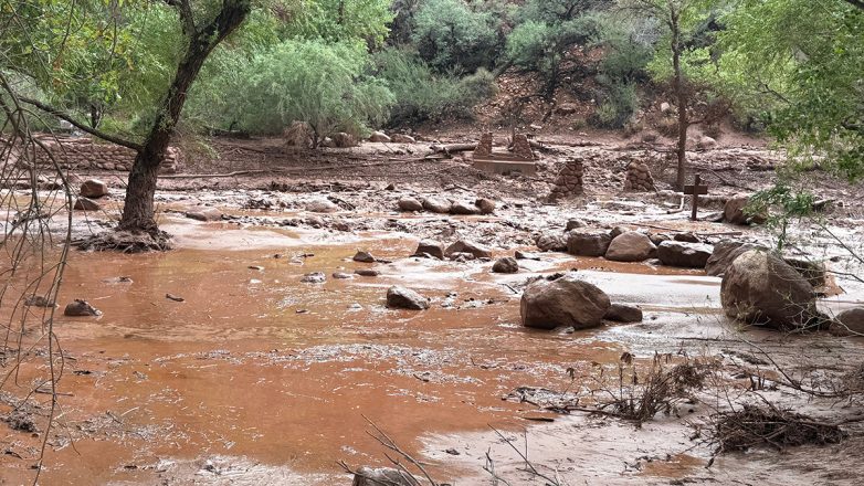Κόκκινο λασπωμένο ποτάμι με πέτρες, δέντρα και υπολείμματα μετά απ…