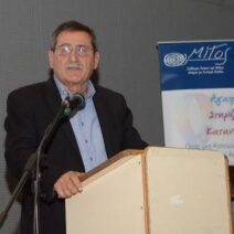 Ο Κ. Πελετίδης μιλάει από βήμα με μικρόφωνο, με πανό για τον αυτισμό…