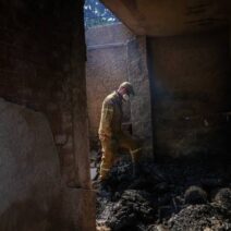 Άνδρας με μάσκα επιθεωρεί το κατεστραμμένο εσωτερικό σπιτιού μετά…