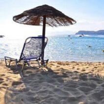 Ηλιόλουστη αμμώδης παραλία με ψάθινη ομπρέλα, μπλε ξαπλώστρα και γ…