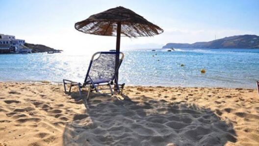 Ηλιόλουστη αμμώδης παραλία με ψάθινη ομπρέλα, μπλε ξαπλώστρα και γ…