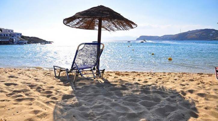 Ηλιόλουστη αμμώδης παραλία με ψάθινη ομπρέλα, μπλε ξαπλώστρα και γ…
