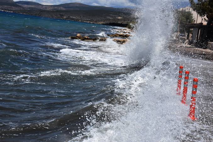 Θυελλώδη κύματα σκάνε στην ακτή και σε δρόμο με κώνους.