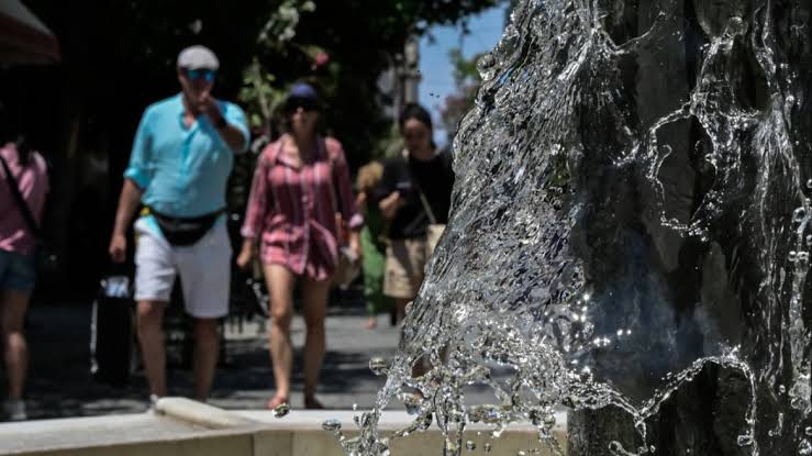 Νερό αναβλύζει από σιντριβάνι σε ηλιόλουστο τοπίο, με ανθρώπους να…