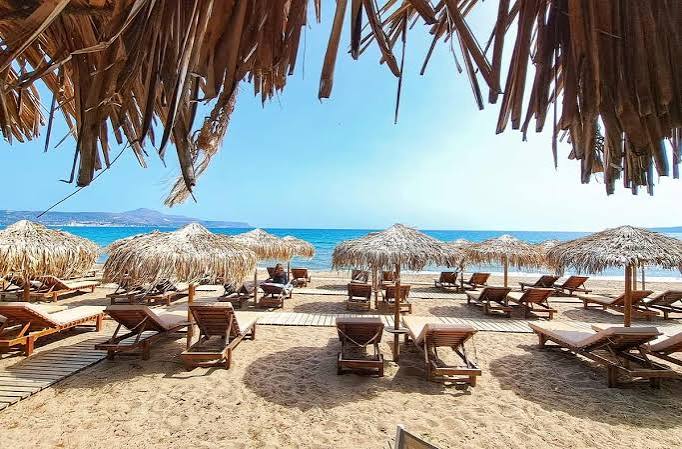 Αχαΐα: Άνοδος της θερμοκρασίας με πιθανότητα βροχής σήμερα 4 Παραλία με ψάθινες ομπρέλες και ξαπλώστρες κάτω από γαλάζιο ουρανό.