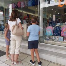 Μητέρα με δύο παιδιά κοιτούν σχολικά είδη σε βιτρίνα καταστήματος …