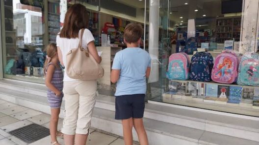 Μητέρα με δύο παιδιά κοιτούν σχολικά είδη σε βιτρίνα καταστήματος …