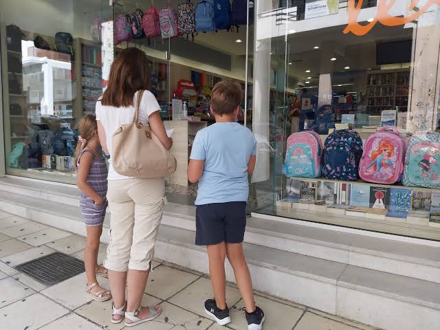 Μητέρα με δύο παιδιά κοιτούν σχολικά είδη σε βιτρίνα καταστήματος …