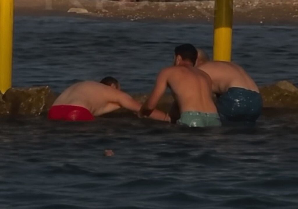 Τρεις άνδρες με μαγιό στο νερό, κοντά σε κίτρινους στύλους, με την π…