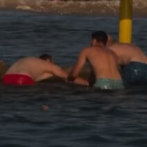 Τρεις άνδρες με μαγιό στο νερό, κοντά σε κίτρινους στύλους, με την π…
