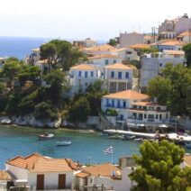 Λιμάνι Σκιάθου με λευκά σπίτια σε πλαγιά, βάρκες στη θάλασσα και ελ…