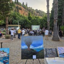 Εξωτερική έκθεση ζωγραφικής με κοινό, φοίνικες και οθόνη προβολής …
