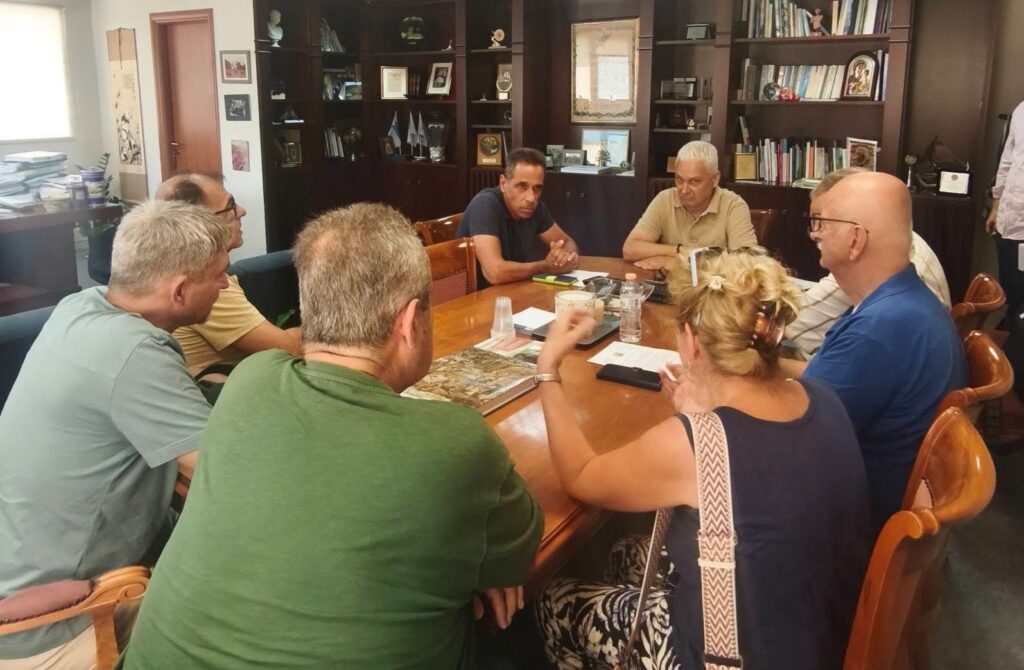 Άτομα σε σύσκεψη γύρω από τραπέζι σε γραφείο με βιβλιοθήκη.