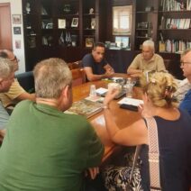 Άτομα σε σύσκεψη γύρω από τραπέζι σε γραφείο με βιβλιοθήκη.