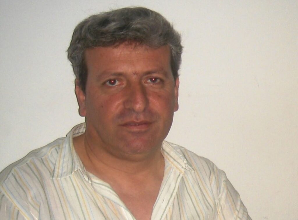Πορτρέτο του Δημήτρη Καρτέρη με γκρίζα μαλλιά και ριγέ πουκάμισο.