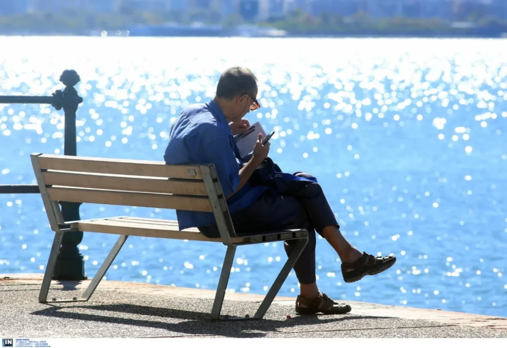 Άνδρας διαβάζει σε παγκάκι με φόντο τη λαμπερή θάλασσα, απολαμβάνο…