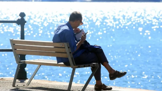 Αχαΐα: Γενικά αίθριος και καλοκαιρινός ο καιρός σήμερα 12 Άνδρας διαβάζει σε παγκάκι με φόντο τη λαμπερή θάλασσα, απολαμβάνο…