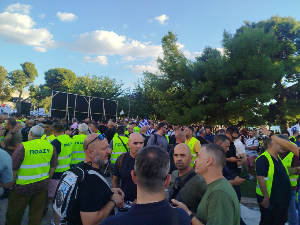 Πλήθος ανδρών με κίτρινα γιλέκα ΠΟΑΣΥ σε εξωτερική συγκέντρωση, με…