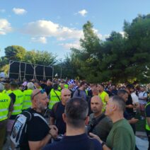 Πλήθος ανδρών με κίτρινα γιλέκα ΠΟΑΣΥ σε εξωτερική συγκέντρωση, με…
