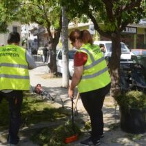 Δύο εργάτες του Δήμου Πατρέων με κίτρινα γιλέκα καθαρίζουν χόρτα σ…