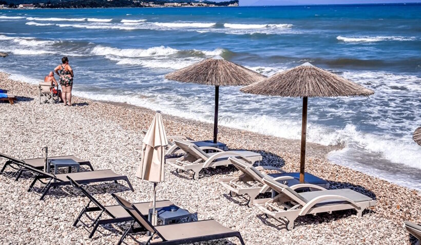 Βοτσαλωτή παραλία με ομπρέλες, ξαπλώστρες και κύματα, με δύο άτομα …