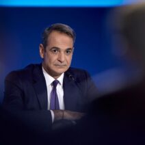 Ο Κυριάκος Μητσοτάκης με σκούρο κοστούμι και γραβάτα, με σταυρωμέν…