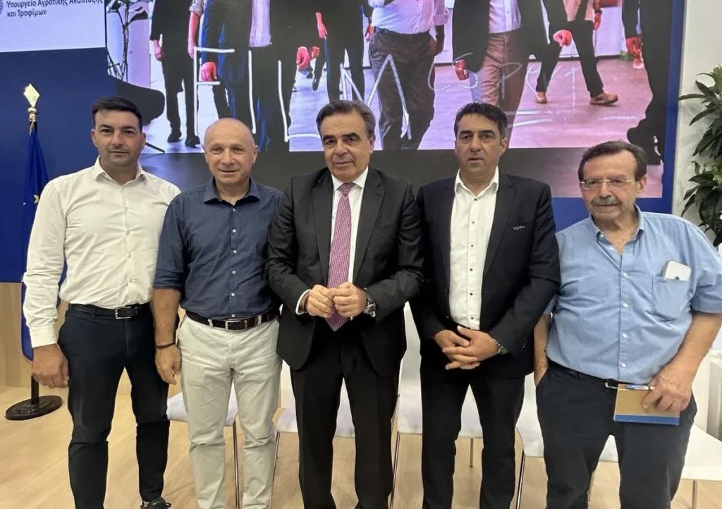 Πέντε άνδρες, συμπεριλαμβανομένου ενός με κοστούμι, στέκονται μπροστά σε οθόνη με το Υπουργείο Αγροτικής Ανάπτυξης και Τρο…
